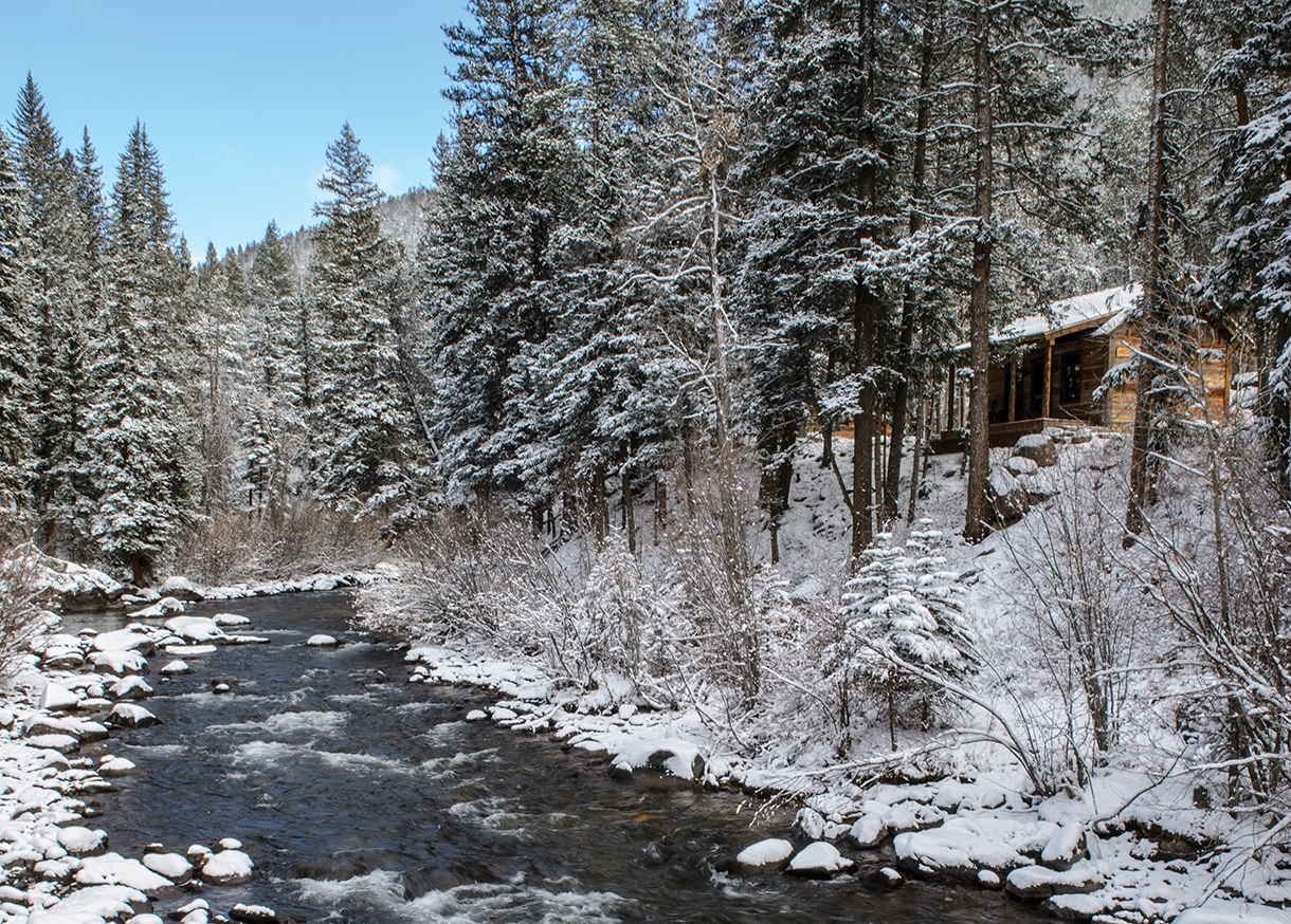 Snowy cabin in the mountains with a river running next to it